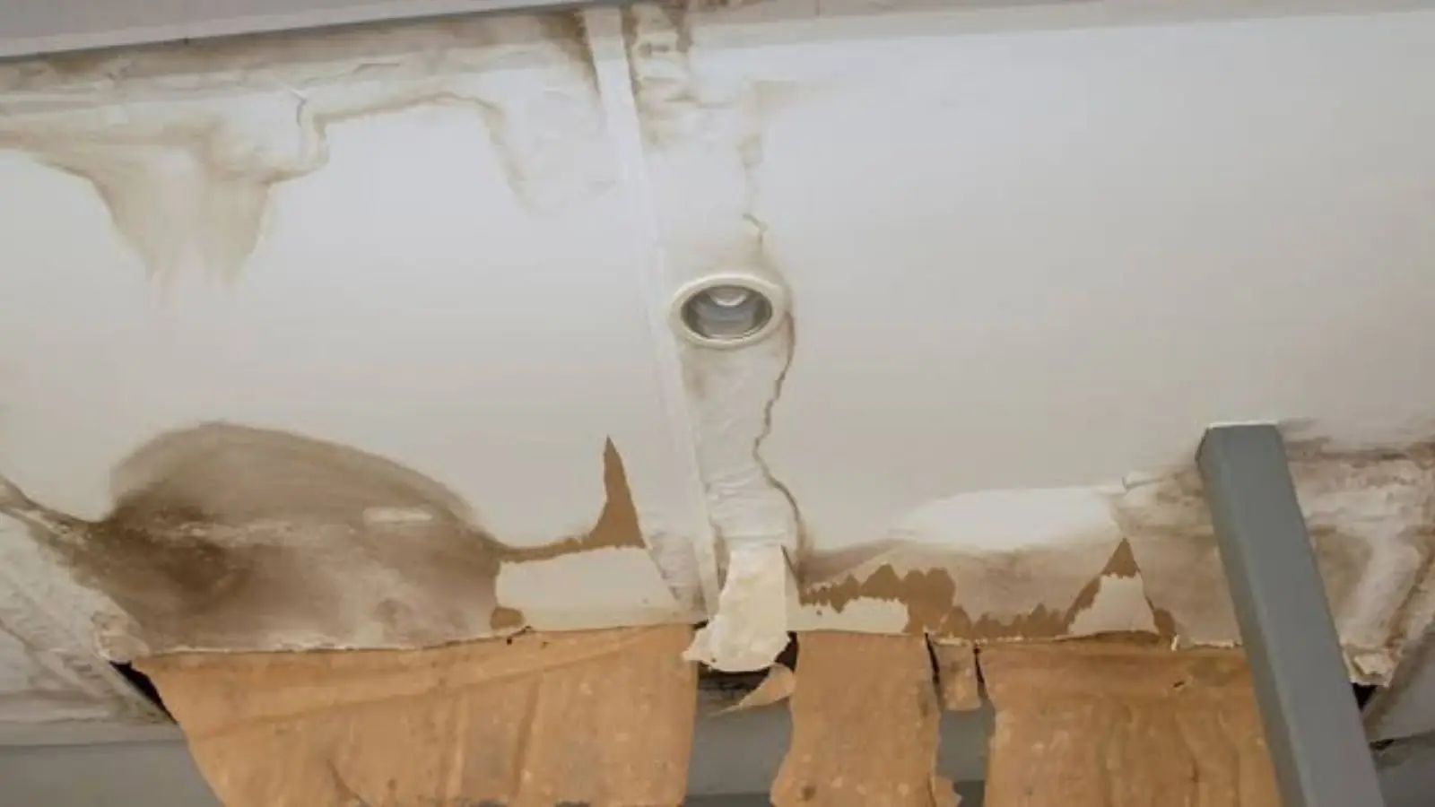 Ceiling with a damaged section around a fixture and exposed backing paper