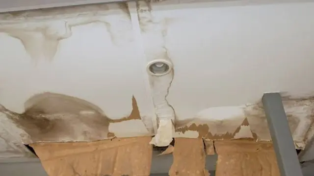 Ceiling with a damaged section around a fixture and exposed backing paper